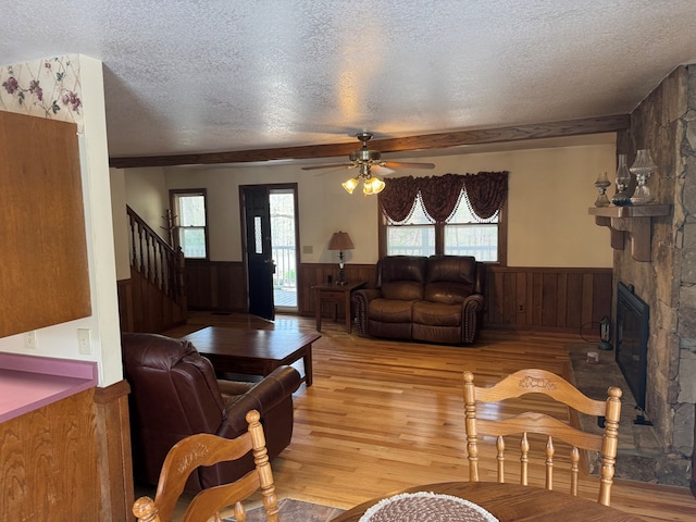 living area with stairway, a ceiling fan, light wood-style floors, wainscoting, and a textured ceiling