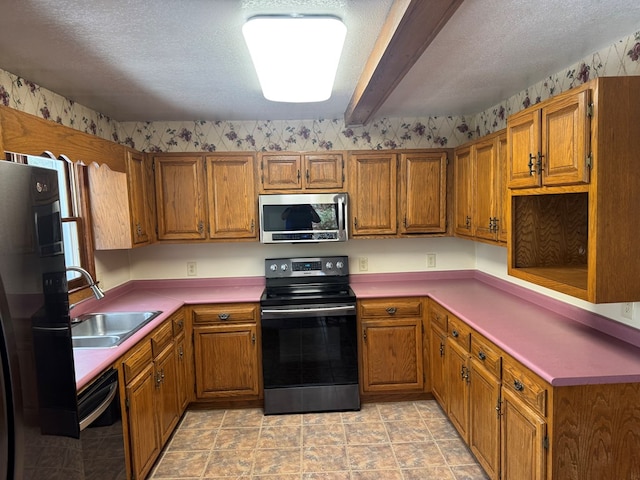 kitchen with a sink, wallpapered walls, a textured ceiling, brown cabinetry, and appliances with stainless steel finishes