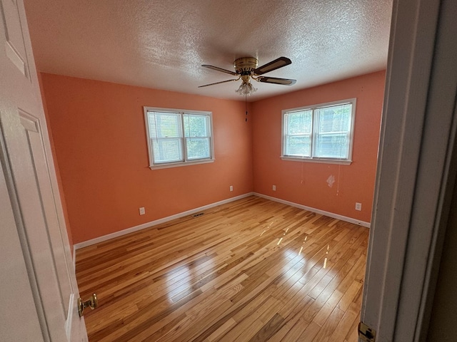 spare room featuring a textured ceiling, light wood finished floors, a wealth of natural light, and ceiling fan