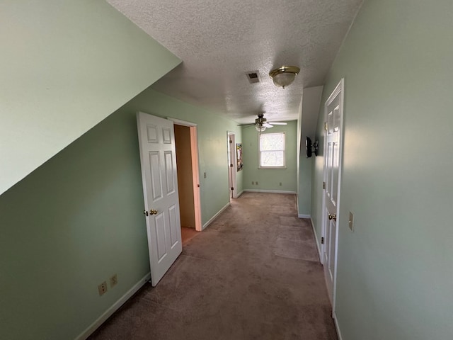 corridor featuring baseboards, carpet floors, visible vents, and a textured ceiling