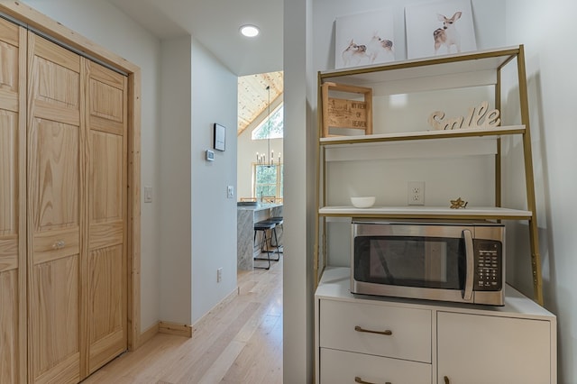 corridor featuring a chandelier, vaulted ceiling, and light hardwood / wood-style flooring