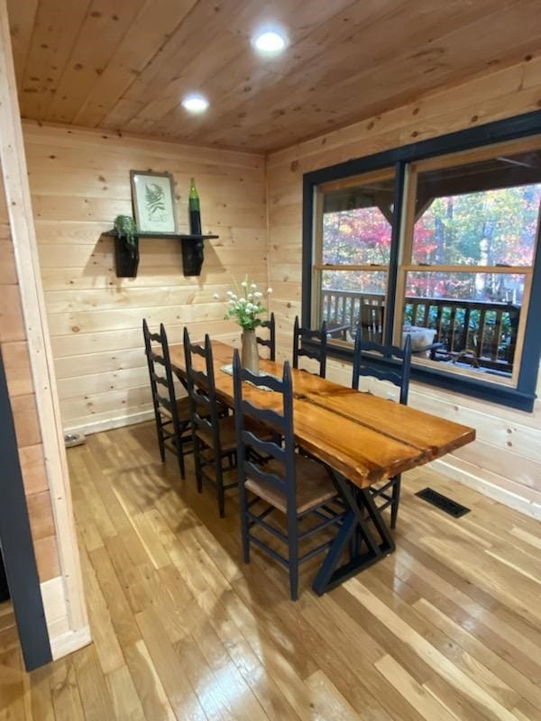 dining space with wood walls, wooden ceiling, and light hardwood / wood-style flooring