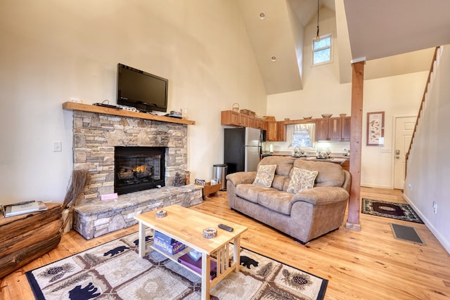 living area with a fireplace, visible vents, high vaulted ceiling, light wood-type flooring, and baseboards