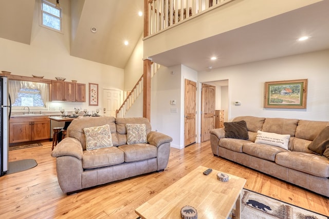 living room featuring a high ceiling, stairway, light wood-type flooring, and recessed lighting