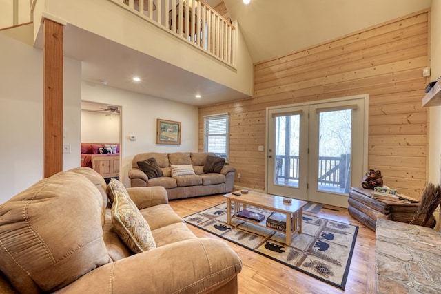 living area with a wealth of natural light, wooden walls, a towering ceiling, and wood finished floors