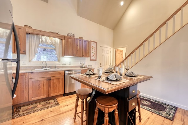 kitchen with stainless steel appliances, high vaulted ceiling, light wood-type flooring, and a sink