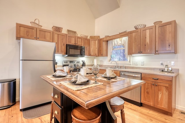 kitchen with high vaulted ceiling, a sink, light countertops, appliances with stainless steel finishes, and light wood-type flooring