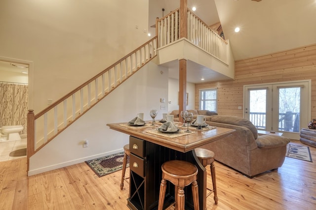 living area with light wood-style floors, wooden walls, a high ceiling, and stairway