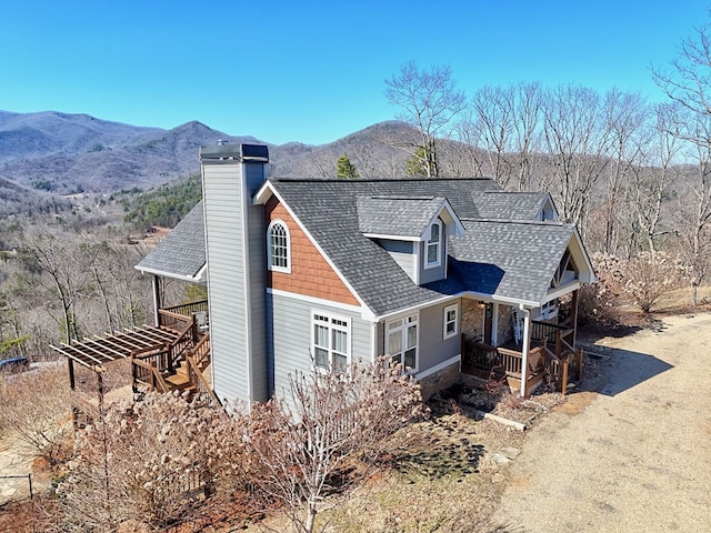 view of front of house featuring a shingled roof, a chimney, a mountain view, and stairs