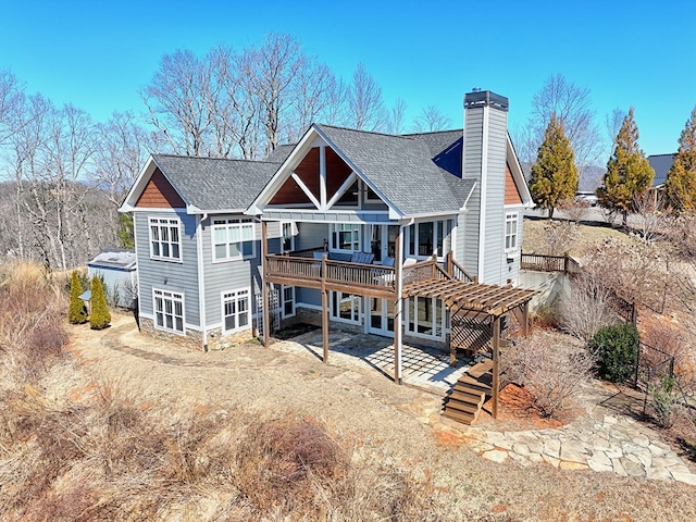 back of property featuring stone siding, roof with shingles, a wooden deck, a chimney, and a patio area