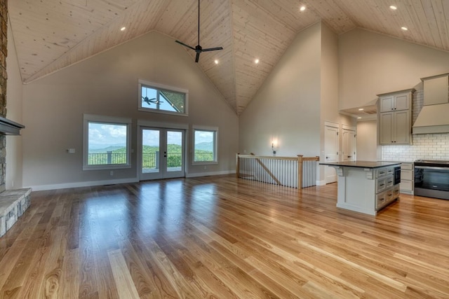 unfurnished living room with high vaulted ceiling, a fireplace, a ceiling fan, baseboards, and light wood-style floors