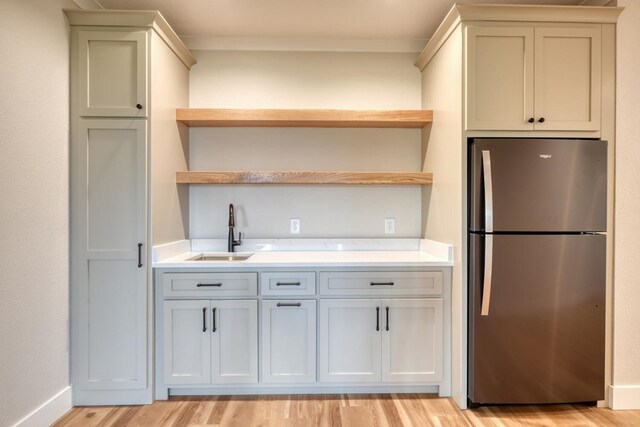 kitchen featuring freestanding refrigerator, light countertops, open shelves, and a sink