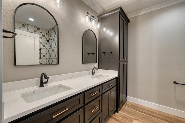 full bath with double vanity, wood finished floors, baseboards, and a sink