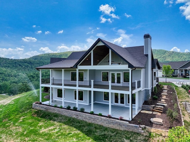 rear view of house featuring a mountain view, french doors, a chimney, a balcony, and a patio area