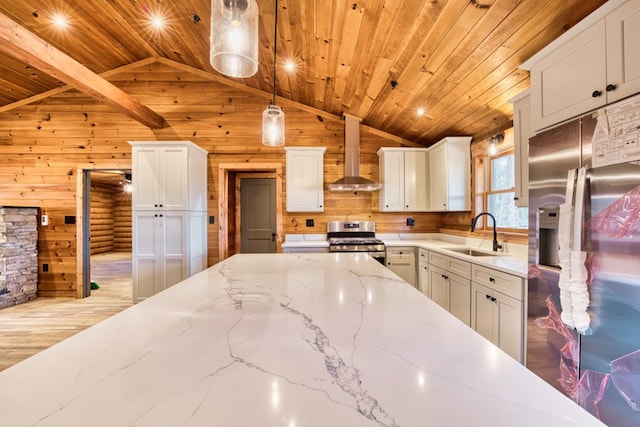 kitchen with pendant lighting, wood walls, sink, wall chimney exhaust hood, and stainless steel appliances