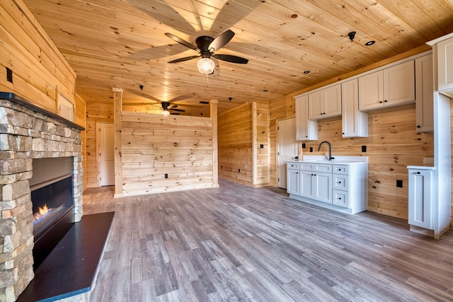 kitchen with a fireplace, wooden ceiling, white cabinets, light hardwood / wood-style floors, and wood walls