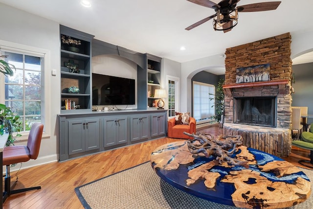 living room featuring a stone fireplace, light hardwood / wood-style floors, ceiling fan, and built in features