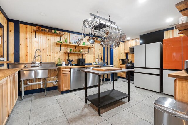 kitchen with light tile patterned flooring, appliances with stainless steel finishes, wood counters, wood walls, and sink