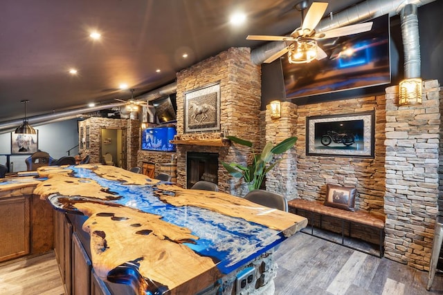 dining space with a stone fireplace, light wood-type flooring, and ceiling fan