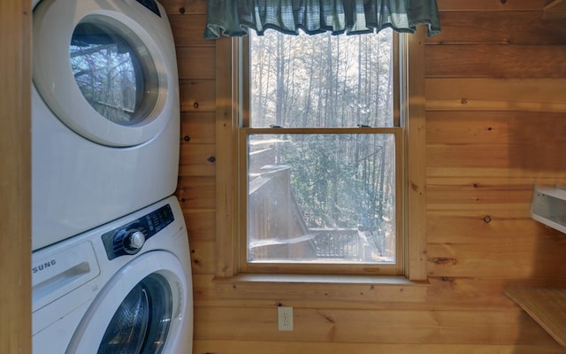 laundry area with plenty of natural light, stacked washer / drying machine, and wood walls