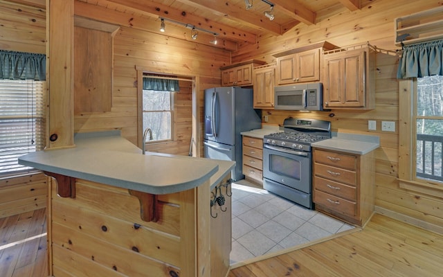 kitchen featuring appliances with stainless steel finishes, a kitchen breakfast bar, kitchen peninsula, and wood walls