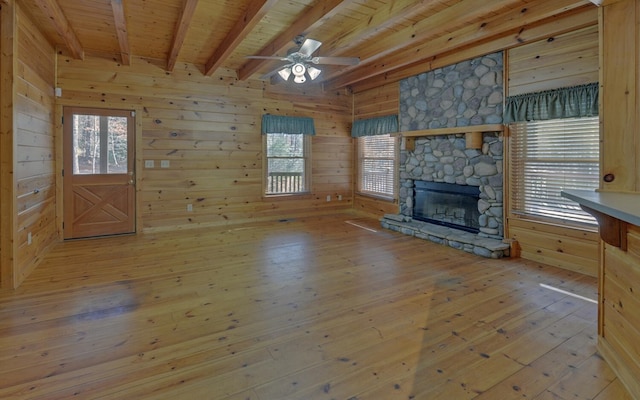 unfurnished living room featuring wooden walls, a stone fireplace, light hardwood / wood-style flooring, and wooden ceiling