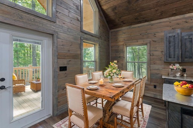 dining area with dark hardwood / wood-style flooring, wood walls, a healthy amount of sunlight, and vaulted ceiling