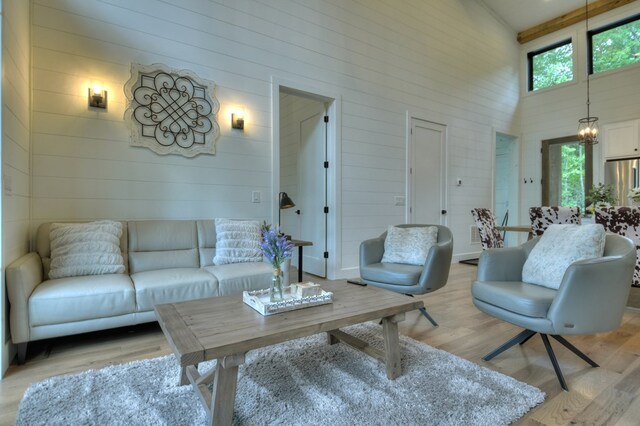 living room featuring light hardwood / wood-style flooring, high vaulted ceiling, a chandelier, and wooden walls