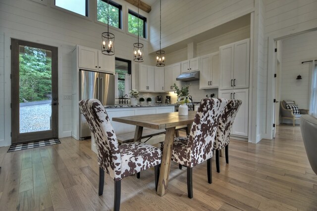 dining room with wood walls, light hardwood / wood-style flooring, a chandelier, and a high ceiling