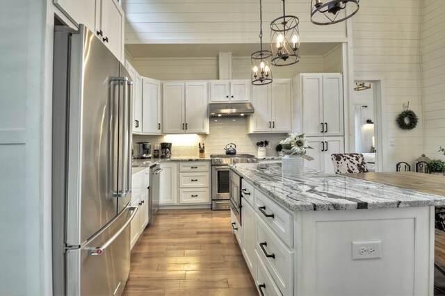 kitchen with white cabinetry, stainless steel appliances, a kitchen island, an inviting chandelier, and light hardwood / wood-style floors