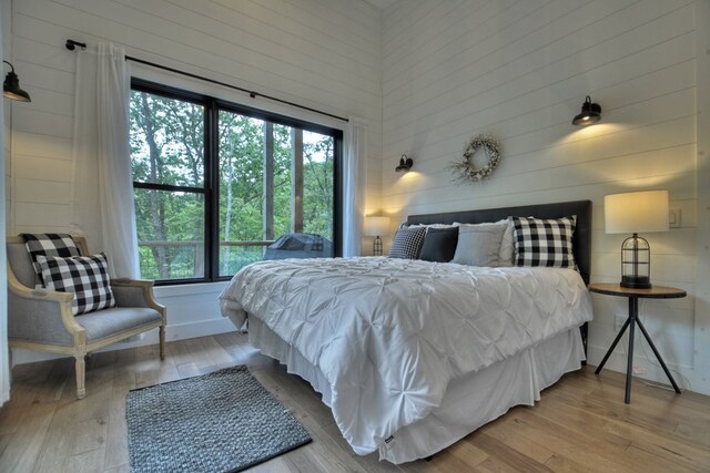 bedroom featuring wood walls, wood-type flooring, and multiple windows