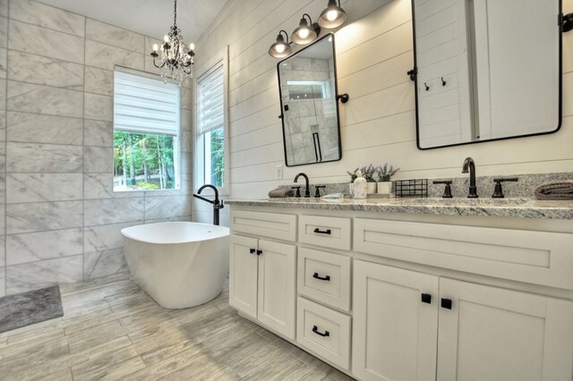 bathroom featuring a notable chandelier, vanity, a washtub, wood-type flooring, and tile walls