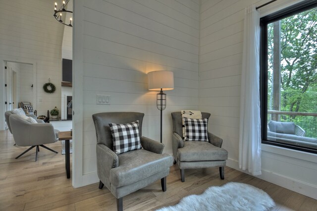 sitting room featuring light hardwood / wood-style flooring, wooden walls, and a chandelier