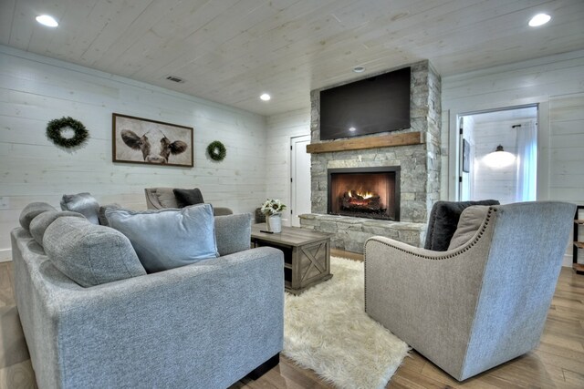 living room featuring light wood-type flooring, wooden ceiling, wooden walls, and a stone fireplace