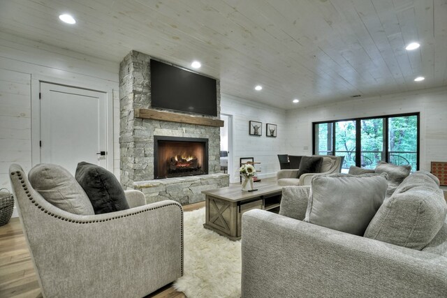 living room with light hardwood / wood-style flooring, wood ceiling, wooden walls, and a stone fireplace