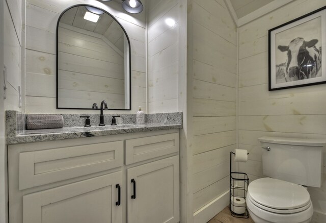 bathroom with wood walls, toilet, and vanity