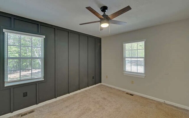 unfurnished room with ceiling fan, light colored carpet, a decorative wall, baseboards, and visible vents