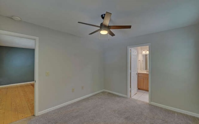 unfurnished bedroom with baseboards, ensuite bathroom, a ceiling fan, and light colored carpet