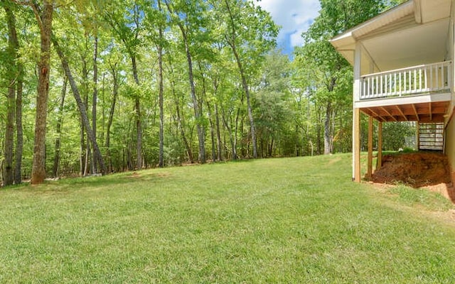 view of yard featuring a view of trees, a wooden deck, and stairs