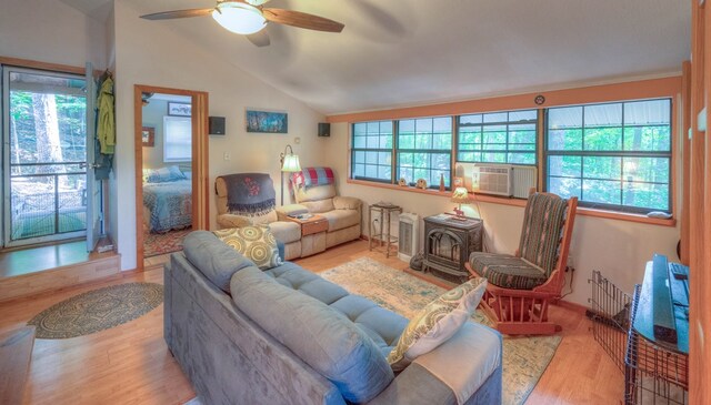 living room with a wood stove, cooling unit, lofted ceiling, ceiling fan, and light wood-type flooring