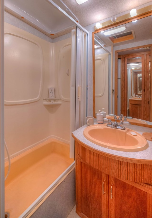 bathroom featuring a textured ceiling, vanity, and walk in shower