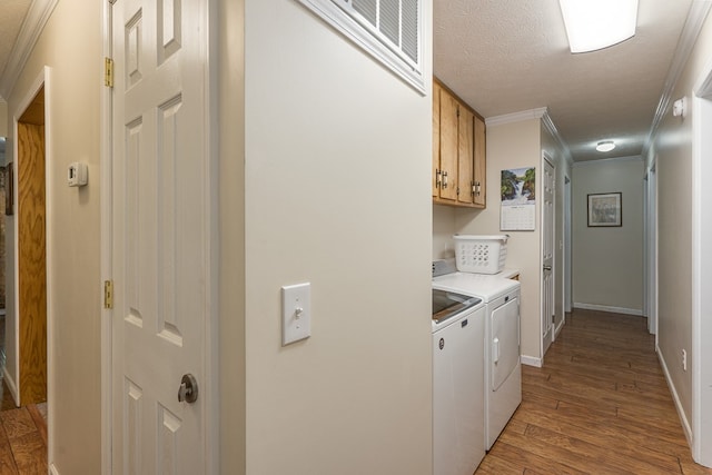 clothes washing area with wood-type flooring, ornamental molding, separate washer and dryer, cabinets, and a textured ceiling