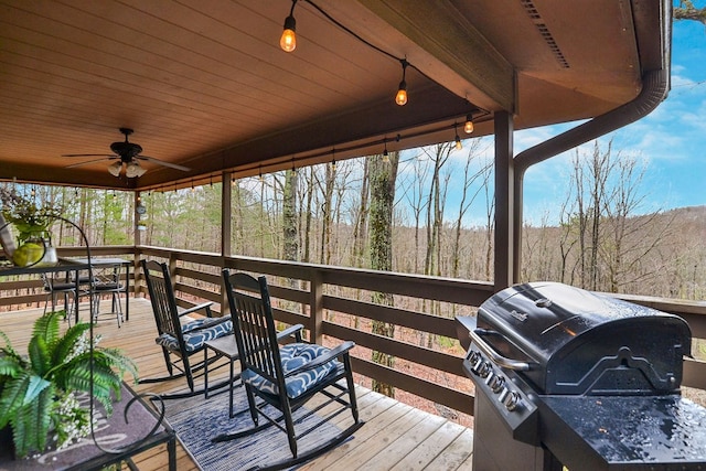 wooden deck featuring a view of trees, a ceiling fan, and grilling area