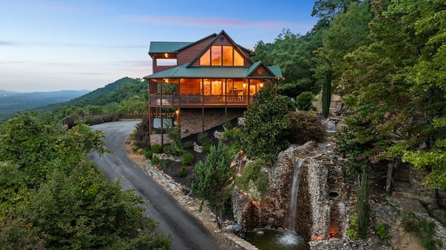 back of property featuring dirt driveway, metal roof, a wooden deck, and a view of trees