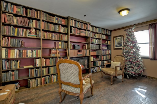 living area featuring wall of books and wood finished floors