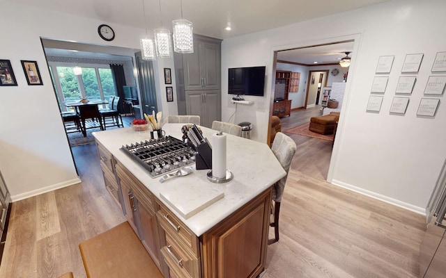 kitchen featuring pendant lighting, light hardwood / wood-style floors, stainless steel gas cooktop, a kitchen island, and ceiling fan with notable chandelier