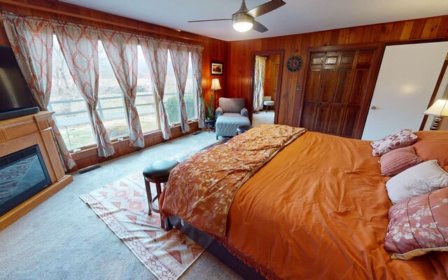 carpeted bedroom featuring ceiling fan and wood walls