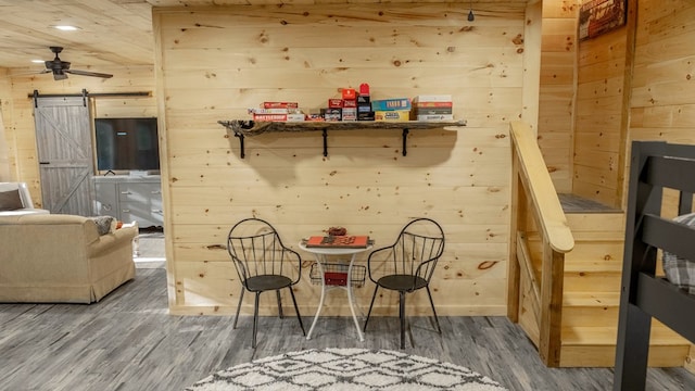 dining space with dark wood-type flooring, wood walls, and a barn door