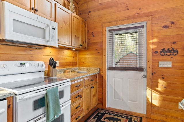 kitchen featuring white appliances, wooden walls, light stone countertops, and brown cabinetry