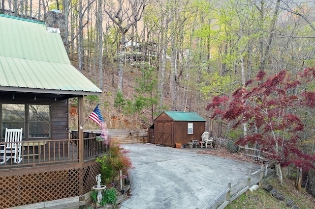 view of yard with a storage unit, a deck, an outdoor structure, fence, and a forest view